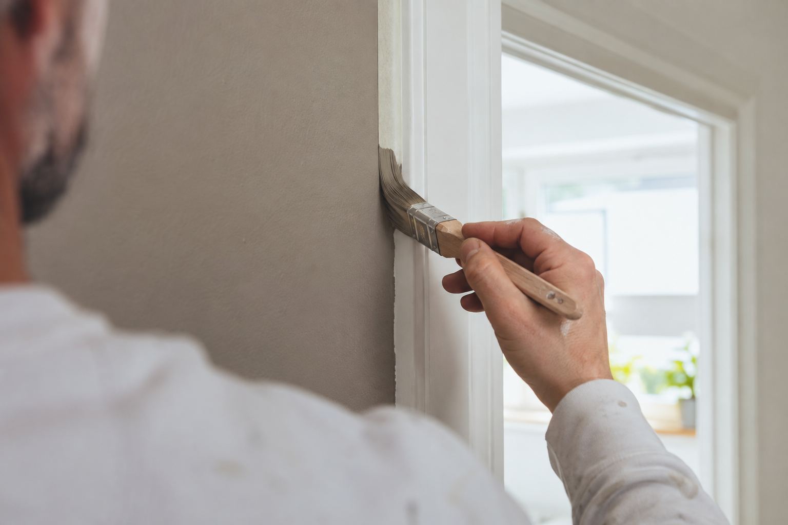 Maler zieht mit dem Pinsel eine saubere Kante am Fensterrahmen